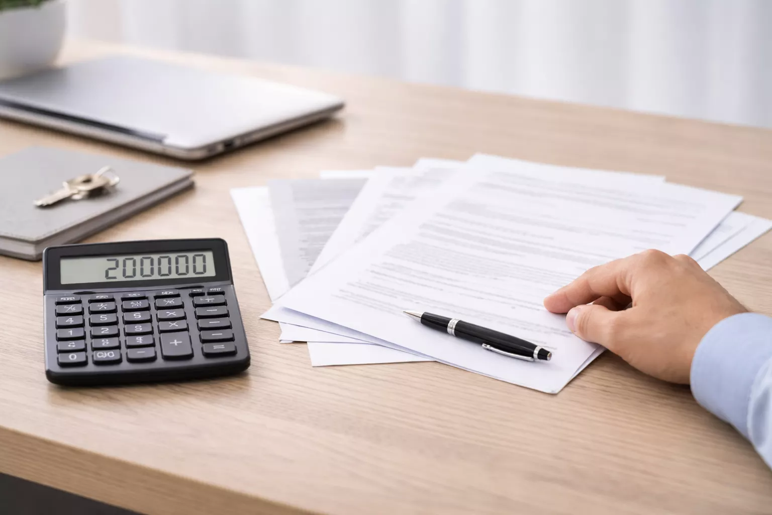 Laskin, asiakirjoja ja käsi työpöydällä havainnollistamassa 200 000 euron perintöveron laskemista